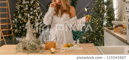 Woman Kitchen Christmas decor in white shirt, peeling tangerines. Illustrating New Year's mood holiday preparations 115543887
