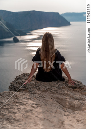 A woman with long hair sits on a rock overlooking the ocean. The scene is peaceful and serene, with the woman taking in the beauty of the landscape. 115543889