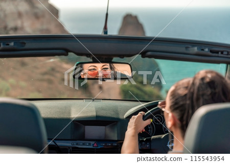 A woman is driving a convertible car with the top down, enjoying the ocean view. The car is red and black, and the woman is wearing a pink shirt. A woman is driving a convertible car with the top down, enjoying the ocean view. The car is red and black, and the woman is wearing a pink shirt. 115543954