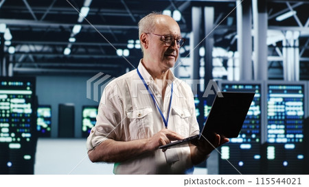 Focused IT professional navigating network of blade servers in industrial hub. Serviceman with laptop ensuring optimum operations, doing optimizations and maintenance in data center Focused IT professional navigating network of blade servers in industrial hub. Serviceman with laptop ensuring optimum operations, doing optimizations and maintenance in data center 115544021