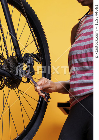 Close up shot of a black woman hand holding specialized spanner for securing and adjusting bike hub and axle. Detailed image showing a wrench being used for bicycle wheel maintenance. 115544061