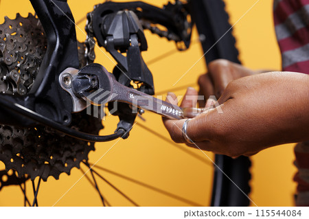 Photo focus on person holding specialized tool for repairs and maintenance of broken bicycle. Close up view of african american hands adjusting various components with precision and expertise. 115544084