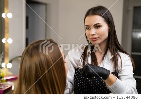 A beautician applies brow lamination to a client in a beauty salon A beautician applies brow lamination to a client in a beauty salon 115544086