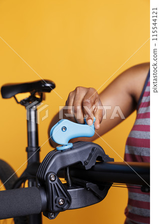 African american individual repairing a damaged bicycle by adjusting clamp on workstand for precision. Close-up of black woman hand grasping bike repair-stand in preparation for maintenance. African american individual repairing a damaged bicycle by adjusting clamp on workstand for precision. Close-up of black woman hand grasping bike repair-stand in preparation for maintenance. 115544121