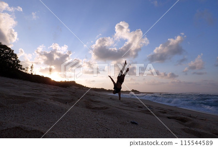 Man does one hand Handstand on beach at sunset 115544589