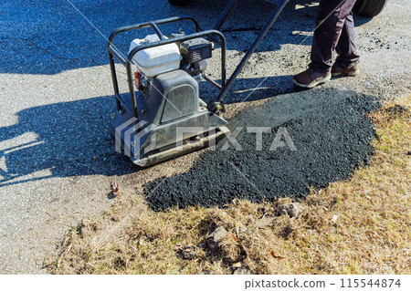 Parking lot repair job necessitates manual tamping compacting vibratory of asphalt with tamping machine 115544874