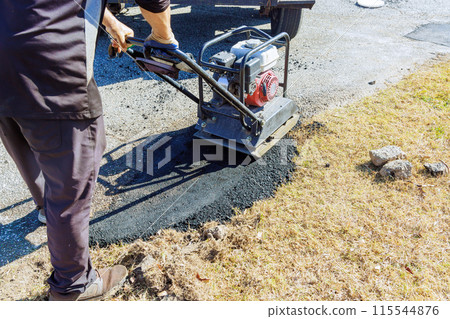 Manual tamping of asphalt using tamping compacting vibratory at parking lot repair Manual tamping of asphalt using tamping compacting vibratory at parking lot repair 115544876