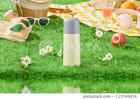 Picnic layout on green grass along the lake scene, from front angle. An unlabeled bottle placed in the middle, dotted with a few tana chrysanthemums, picnic tools decoration in back 115549814