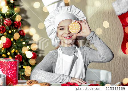Cheerful girl closes her eye with Christmas gingerbread cookies in the shape of a ball. 115553169