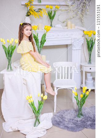 Cute girl in a yellow dress with a bouquet of purple flowers on a background of yellow tulips. 115553191