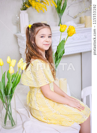 A cute girl in a yellow dress with a bouquet of yellow tulips against the background of bouquets of yellow tulips. 115553192