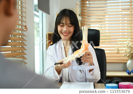 Professional orthopedic doctor explaining to patient about treatment, pointing at model of ankle and foot bones 115553679