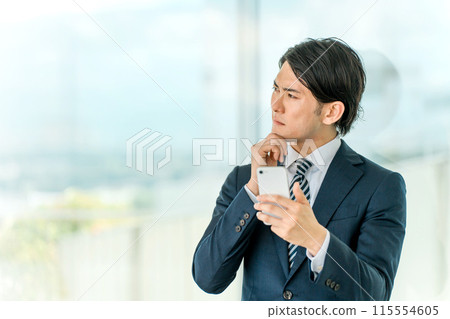 一位身穿西裝的年輕亞洲商人拿著智慧型手機思考和擔憂（職業轉變、策略、獨立、創業） 115554605