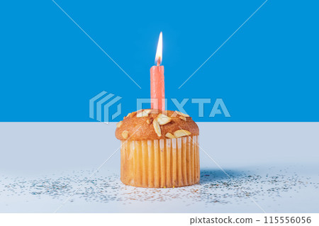 Birthday cupcake with glowing candles on white table with blue background. Closeup Birthday cupcake with glowing candles on white table with blue background. Closeup 115556056