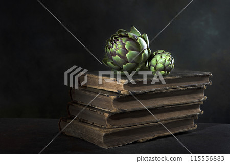 An artichoke and an old book. Artichoke is lying on the book. Dark background. Vintage old book. An artichoke and an old book. Artichoke is lying on the book. Dark background. Vintage old book. 115556883
