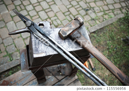 blacksmith's hammer and tongs lying on an anvil . Outdoor forge 115556956