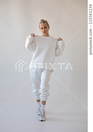 Beautiful blonde girl in a white hoodie and tights posing on a white background 115561239