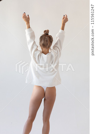 Beautiful blonde girl in a hoodie and panties posing with her back on a white background 115561247