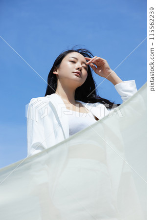 Portrait of a young woman wearing a white jacket, photographed against the sky Portrait of a young woman wearing a white jacket, photographed against the sky 115562239
