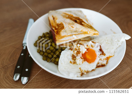 breakfast scrambled eggs hot sandwich with ham and cheese, green peas, legumes on plate breakfast scrambled eggs hot sandwich with ham and cheese, green peas, legumes on plate 115562651