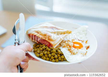 breakfast scrambled eggs hot sandwich with ham and cheese, green peas, legumes on plate breakfast scrambled eggs hot sandwich with ham and cheese, green peas, legumes on plate 115562652