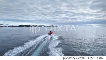 Man riding zodiac red boat in Antarctica polar ocean. Active, outdoor. South Pole travel and exploration. Discover the beauty of wild nature. Cold winter landscape. Aerial drone shot pov back view Man riding zodiac red boat in Antarctica polar ocean. Active, outdoor. South Pole travel and exploration. Discover the beauty of wild nature. Cold winter landscape. Aerial drone shot pov back view 115563387