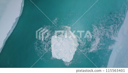 Aerial large iceberg floating blue ocean water in ice canyon. Snow covered glacier melting in Antarctica. Ecology, melting ice, climate change and global warming concept. Static shot top down view 115563401