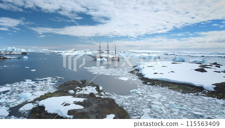 Travel to Antarctica, expedition on wooden yacht. Boat tour South Pole. Explore arctic wild nature in sunny day. Polar ocean, icebergs, blue sky. Winter holiday vacation background. Aerial drone shot 115563409