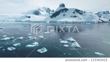 Aerial Antarctica global warming climate change problem. Melting icebergs drifting in water, ice float in polar ocean. Crashed glacier at polar nature environment. Snow covered mountains in background 115563425
