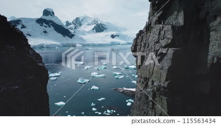 Aerial flight in mountain canyon Antarctica. Majestic snowy mountains towering polar ocean. Cracked glacier icebergs melting floating in cold ocean. Ecology, melting ice, climate change global warming Aerial flight in mountain canyon Antarctica. Majestic snowy mountains towering polar ocean. Cracked glacier icebergs melting floating in cold ocean. Ecology, melting ice, climate change global warming 115563434