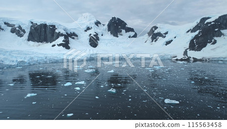 Antarctica snow covered mountains landscape reflected in calm cold water. Glacier towering ice ocean bay. Fly over untouched wilderness of South Pole seascape. Ecology, climate change global warming Antarctica snow covered mountains landscape reflected in calm cold water. Glacier towering ice ocean bay. Fly over untouched wilderness of South Pole seascape. Ecology, climate change global warming 115563458