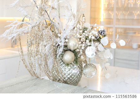 A silver vase with white branches and balls stands on a table in a white kitchen interior 115563586