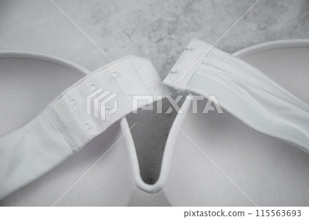 A white bra with hard cups and a push-up is turned upside down, straps and a clasp on a gray background are on the cups of the bra. High quality photo A white bra with hard cups and a push-up is turned upside down, straps and a clasp on a gray background are on the cups of the bra. High quality photo 115563693