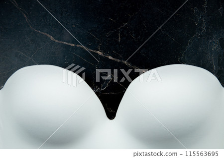 A white bra with stiff cups and a push-up made of white smooth satin fabric lies at the bottom of the photo against a background of black marble. High quality photo A white bra with stiff cups and a push-up made of white smooth satin fabric lies at the bottom of the photo against a background of black marble. High quality photo 115563695