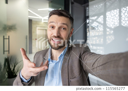 Businessman in a modern office making a video call, smiling and engaging with the camera while gesturing 115565277