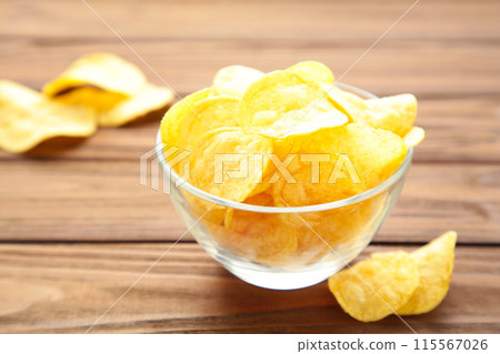 Potato chips on bowl on brown wooden background Potato chips on bowl on brown wooden background 115567026