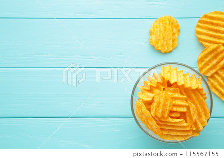 Golden potato chips in bowl on blue wooden background. 115567155