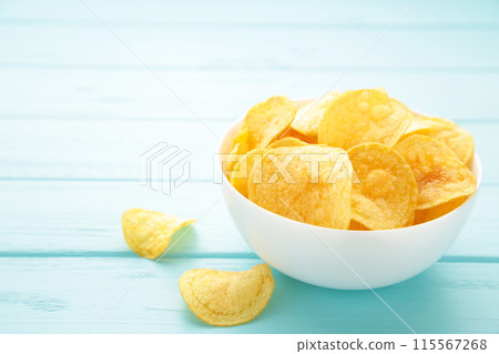 Potato chips on bowl on blue wooden background 115567268