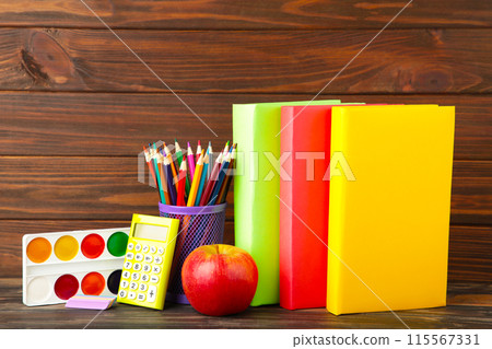 Multi coloured school books and stationery on brown wooden background Multi coloured school books and stationery on brown wooden background 115567331