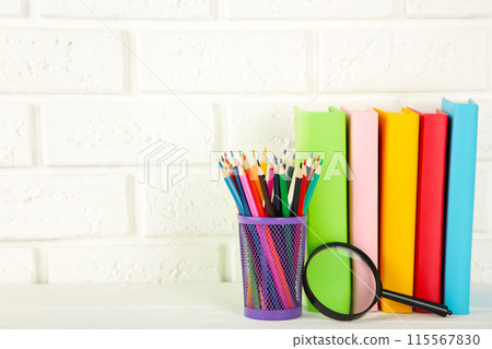 Multi coloured school books and stationery on white brick wall background 115567830