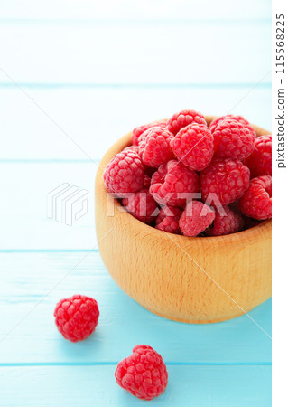 Ripe raspberries in wooden bowl on blue background. Top view 115568225