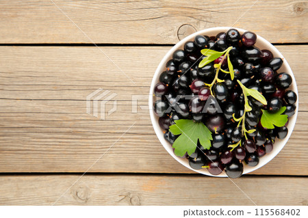Black currant in a white bowl on grey wooden background Black currant in a white bowl on grey wooden background 115568402