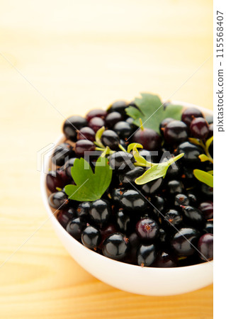Black currant in a white bowl on wooden background 115568407