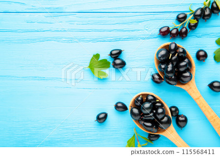 Black currant in wooden spoons on blue background Black currant in wooden spoons on blue background 115568411