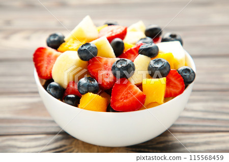 Salad with fresh fruits and berries on brown wooden background Salad with fresh fruits and berries on brown wooden background 115568459