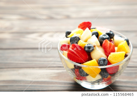 Salad with fresh fruits and berries on brown wooden background 115568465