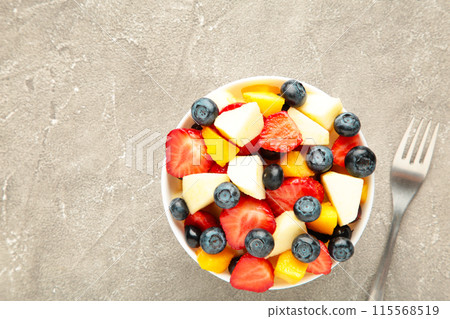 Fruit salad in a bowl with fork, served on grey background. Fruit salad in a bowl with fork, served on grey background. 115568519