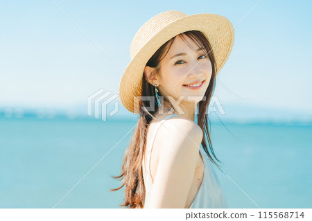 A woman wearing a straw hat with the sea and blue sky in the background 115568714