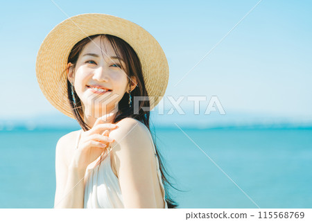 A woman wearing a straw hat with the sea and blue sky in the background A woman wearing a straw hat with the sea and blue sky in the background 115568769