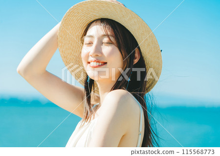 A woman wearing a straw hat with the sea and blue sky in the background 115568773